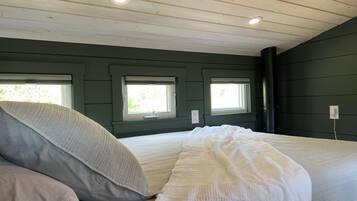 Un dormitorio con una cama, dos ventanas y techo de madera.