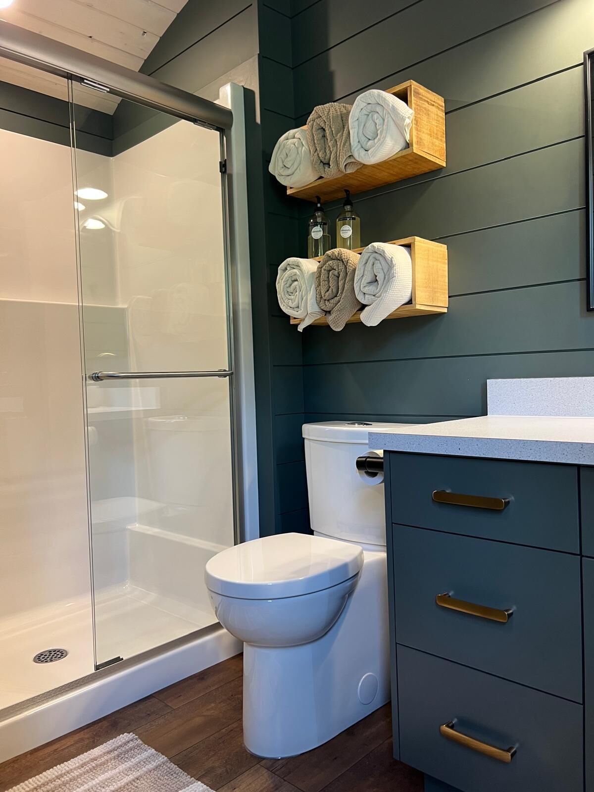 Une salle de bain moderne avec une douche à l’italienne en verre, des toilettes blanches et un meuble-lavabo bleu foncé doté de poignées dorées.