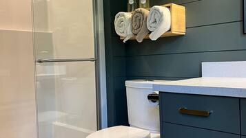 Une salle de bain moderne avec une douche à l’italienne en verre, des toilettes blanches et un meuble-lavabo bleu foncé doté de poignées dorées.
