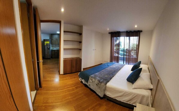 Une chambre avec un lit, un plancher en bois, une vue sur l’extérieur et un escalier menant à une autre pièce.