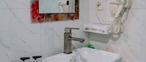 Un baño con lavamanos blanco, un espejo con marco floral, un secador de pelo y dos botellas de gel de ducha.