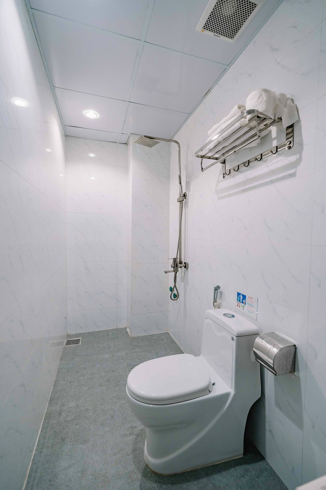 A modern bathroom with a white toilet, a shower with a handheld showerhead, and a towel rack with towels.