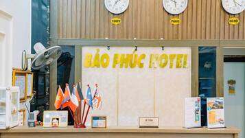 A hotel reception desk with clocks indicating Tokyo, Paris, and Hanoi times, flags, and a reception sign.