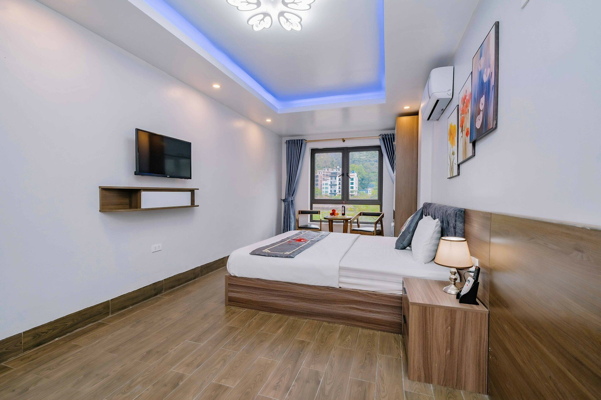 Quarto de hotel moderno com cama, mesa de cabeceira, televisão, obras de arte e janela com cortinas.