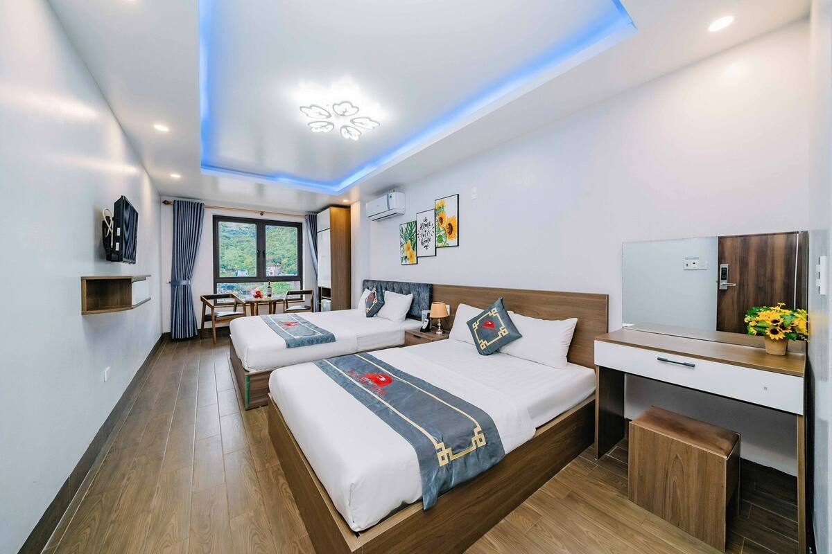 Ein modernes Hotelzimmer mit zwei Betten, einem Schreibtisch, einem Fernseher und einem Fenster mit Blick auf Grünflächen.