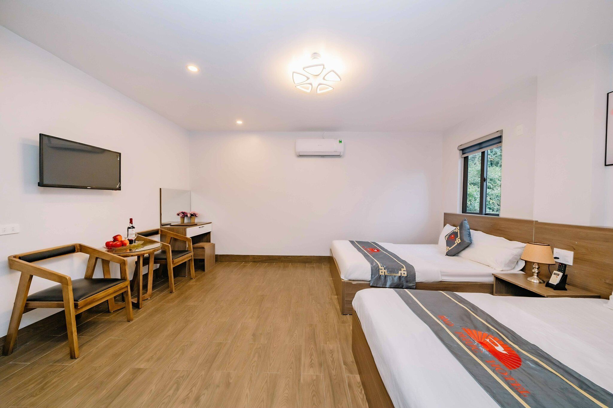 Quarto de hotel com cama, escrivaninha, cadeira, televisão e janela.