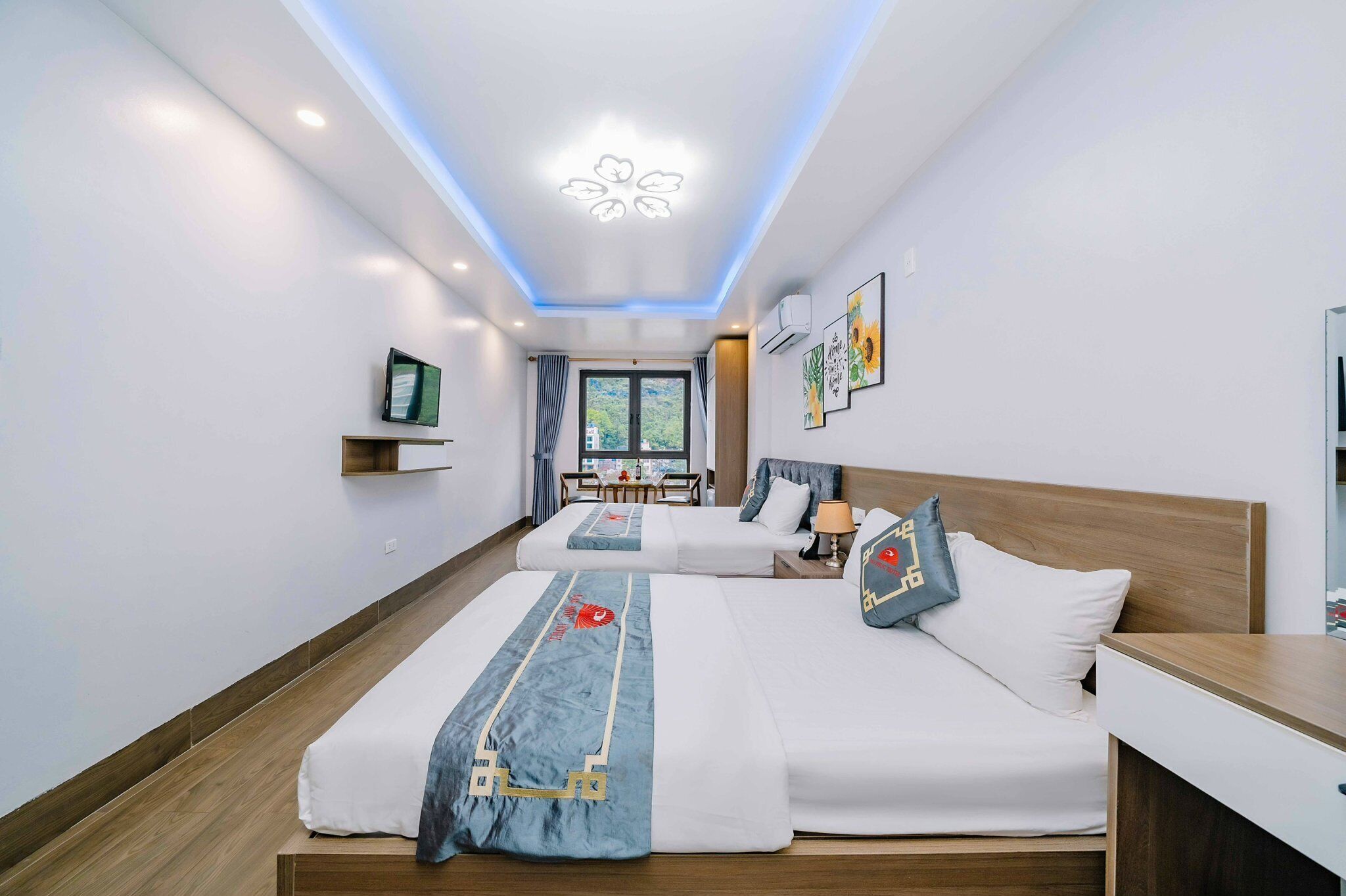 A hotel room with two beds, a desk, a TV, and a window with a view of buildings.