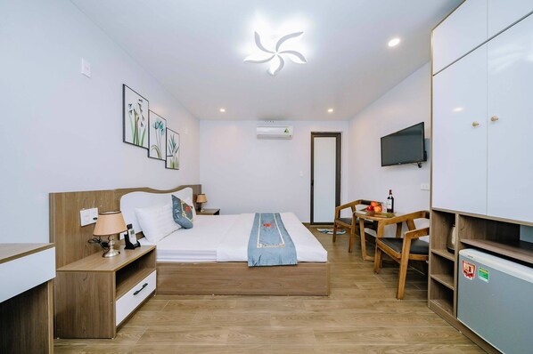 A modern hotel room with a wooden bed, a desk, a chair, a TV, and a mini-fridge. - Bao Phuc Hotel (Hai Phong)
