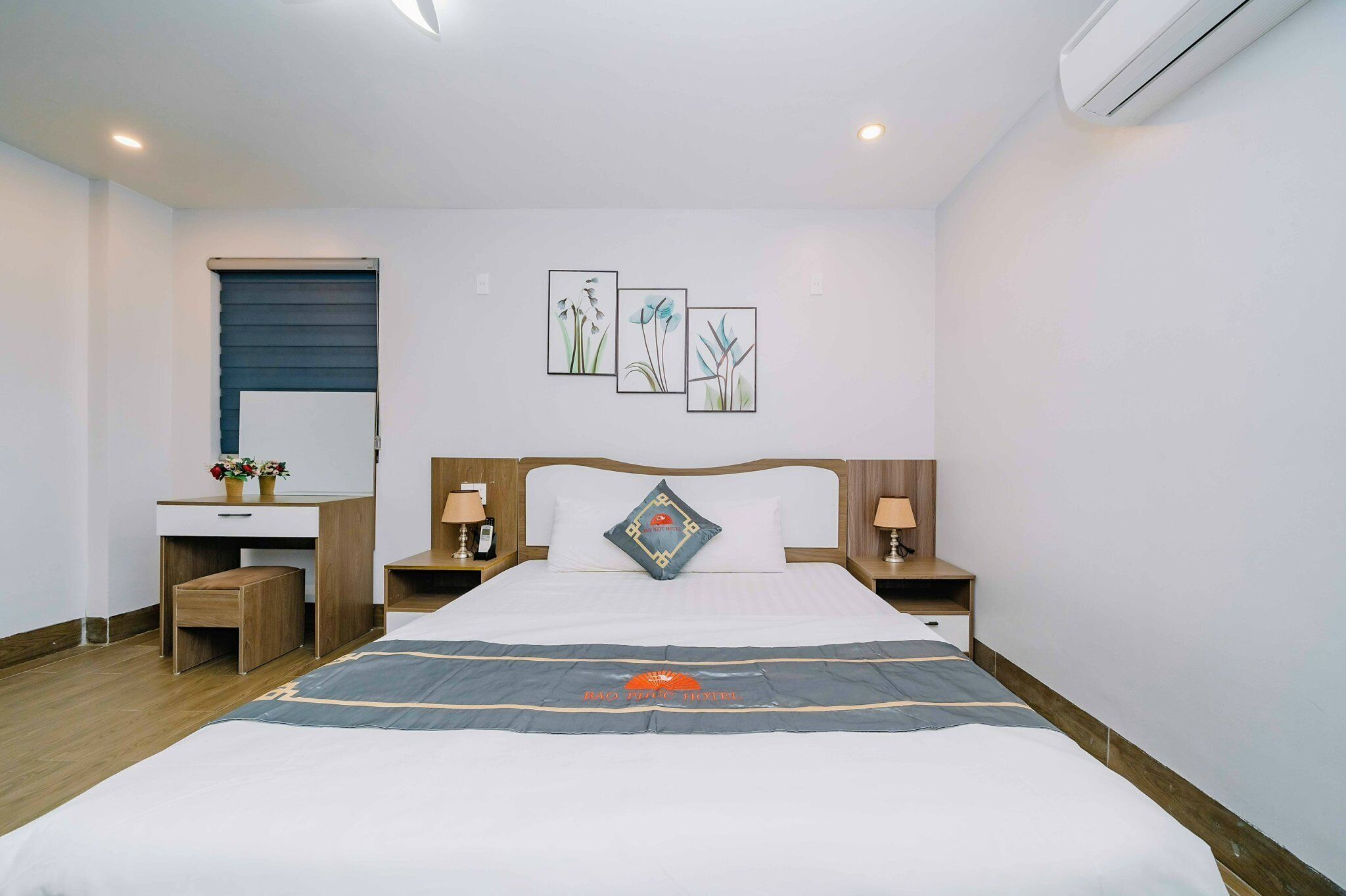 Una habitación de hotel con cama, mesitas de noche, escritorio y ventana con persianas.