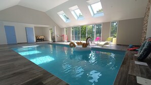 An indoor swimming pool with skylights, a lounge area with chairs, and a view of the outdoors. - 17th-Century Mill with Indoor Pool – Romantic Escape in Brittany (Ploudalmézeau)