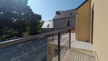 A balcony with a metal railing overlooking a gravel driveway and a stone building with a sloped roof.