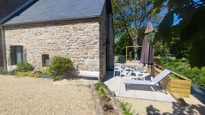 Une maison en pierre avec une allée en gravier, une terrasse dotée de mobilier d’extérieur et une plateforme en bois.