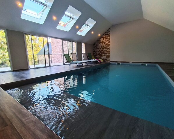 Une piscine intérieure avec des puits de lumière, un mur en pierre et des chaises longues.