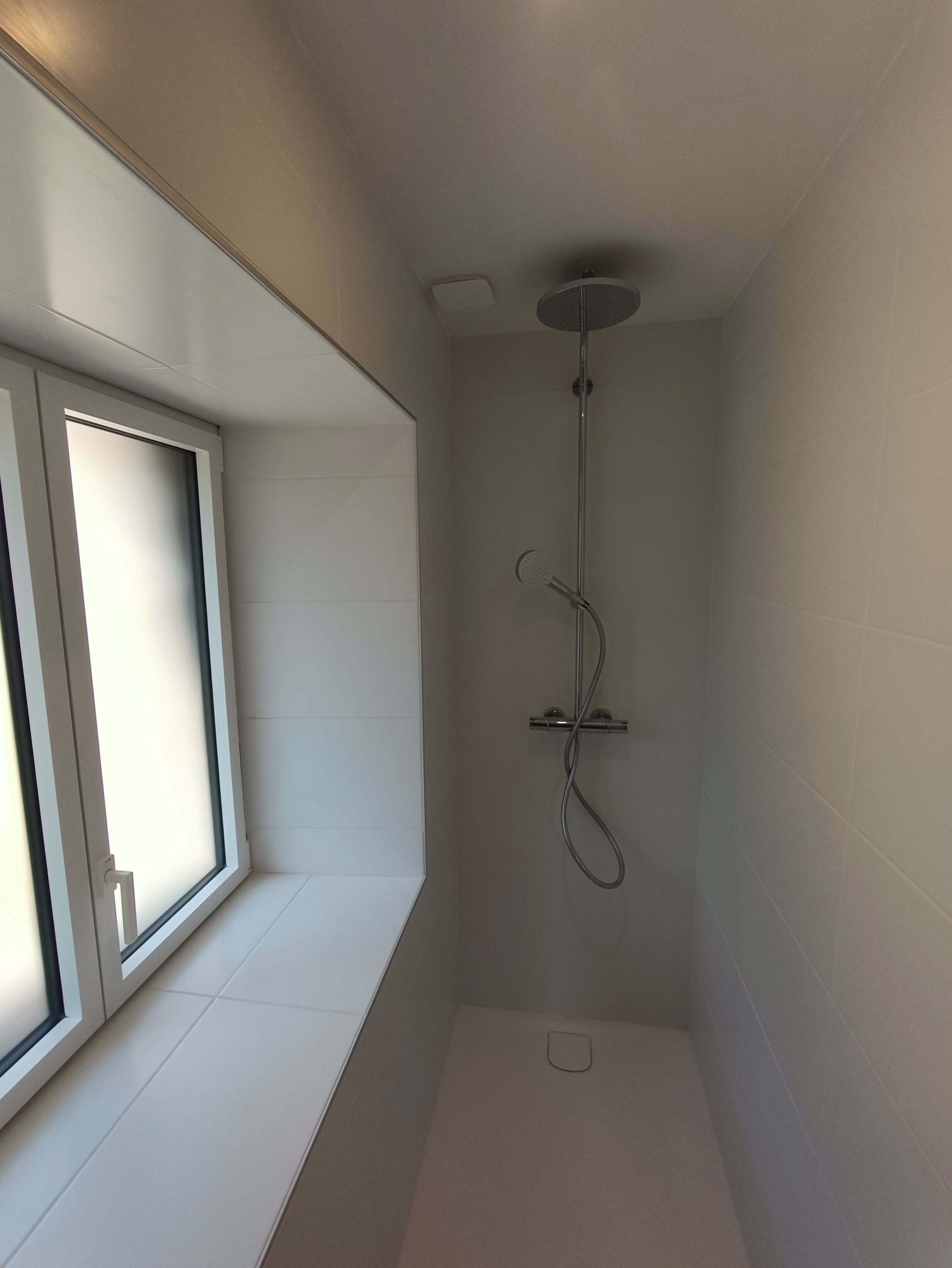 Ein kleines, modernes Duschbad mit Fenster, einer Duschbrause und einer Bedienkonsole.