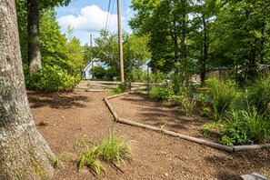 A garden with a wooden fence, various plants, and a house in the background.