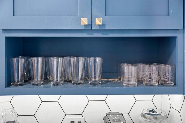 Una cocina con un armario azul que contiene varios vasos de vidrio transparente.