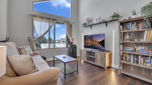 Una sala de estar con sofá, mesa de centro, televisor, estantería y un gran ventanal con cortinas.