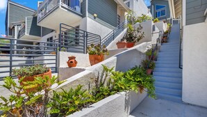 Un edificio residencial con una escalera que lleva a un balcón, rodeado de plantas en macetas.