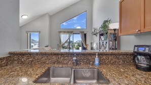 Una cocina con encimeras de granito, un lavamanos doble, una cafetera y un amplio ventanal con vistas al exterior.
