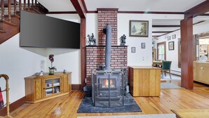 A living room with a brick fireplace, wooden flooring, a wooden staircase, a flat-screen TV, and a dining area. - Pondside Retreat Near Narrowsburg & The Delaware River (Beach Lake)