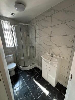 A bathroom with a glass-enclosed shower, a white toilet, and a white sink with cabinets. - Luxe Spacious 5-bed House in Liverpool (Liverpool)
