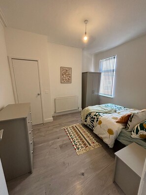 A bedroom with a bed, a wardrobe, a radiator, a door, and a window with blinds. - Luxe Spacious 5-bed House in Liverpool (Liverpool)