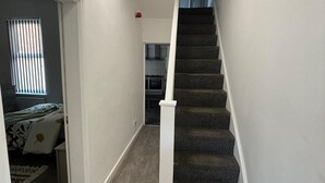 A narrow hallway with a carpeted staircase leading to a kitchen area. - Luxe Spacious 5-bed House in Liverpool (Liverpool)