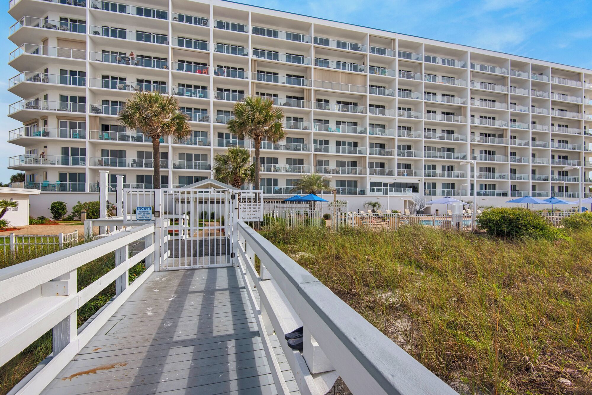 A multi-story hotel with balconies, a pool area, and a boardwalk leading to the entrance.