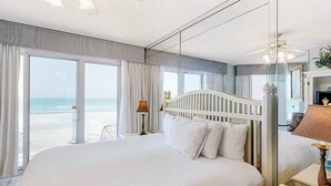 Habitación de hotel con una cama grande, un balcón con vistas a la playa y un espejo amplio que refleja la habitación.