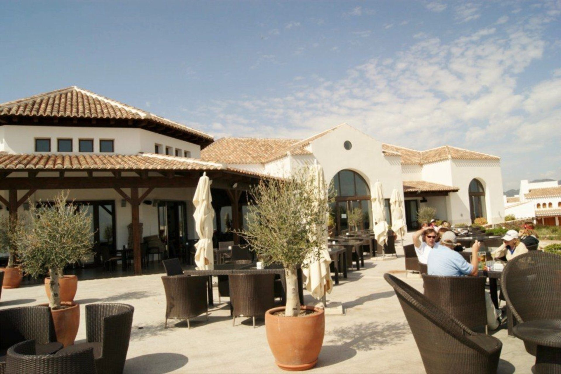 An outdoor patio area with wicker furniture, potted plants, and a building with a tiled roof.
