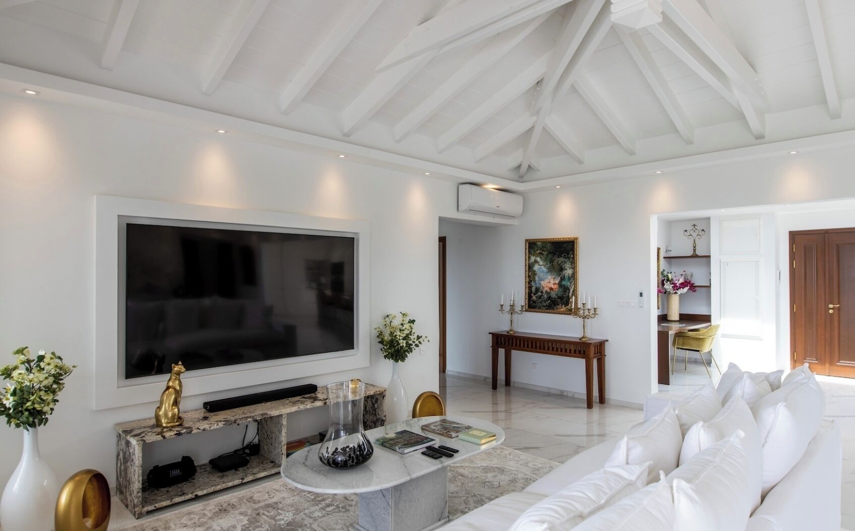 A modern living room with a large flat-screen TV, a marble coffee table, a white sofa, and a console table with decorative items.