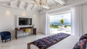 Een moderne hotelkamer met een groot bed, een bureau met een televisie, een gele stoel en uitzicht op de oceaan.