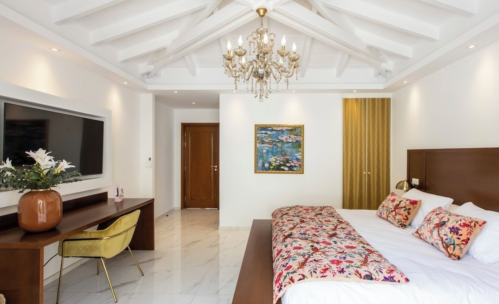 Un dormitorio moderno con una cama grande, un escritorio, un televisor y una araña.