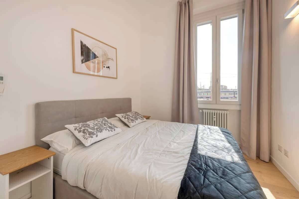 Ein Schlafzimmer mit einem Bett, einem Nachttisch, einem Fenster mit Vorhängen und Blick auf die Stadt.