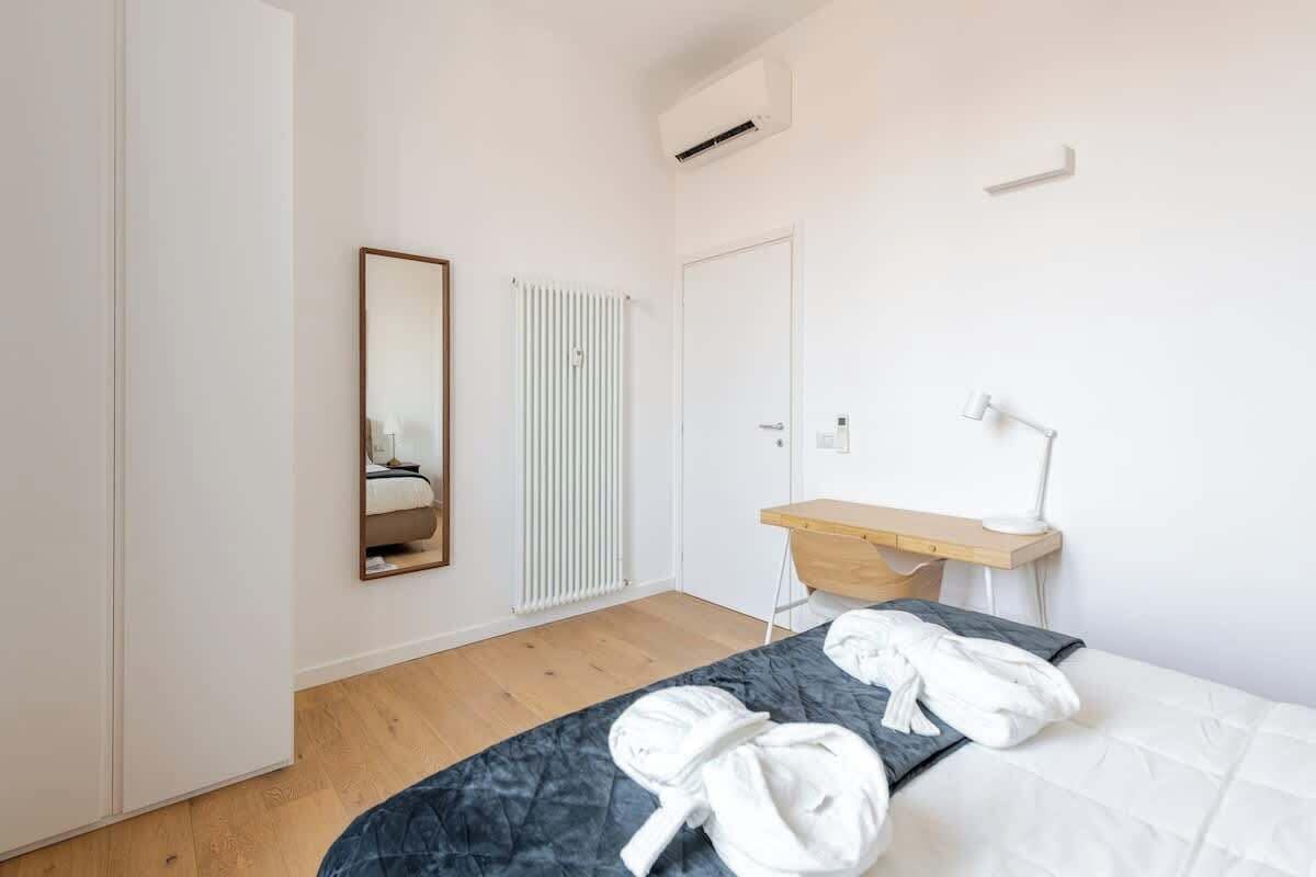 Une chambre à coucher comprenant un lit, une table de chevet, un miroir, un radiateur et une armoire.
