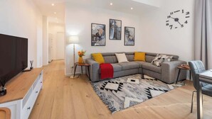 Una sala de estar moderna con un sofá gris, un televisor de pantalla plana, una mesa de centro de madera y una alfombra estampada.