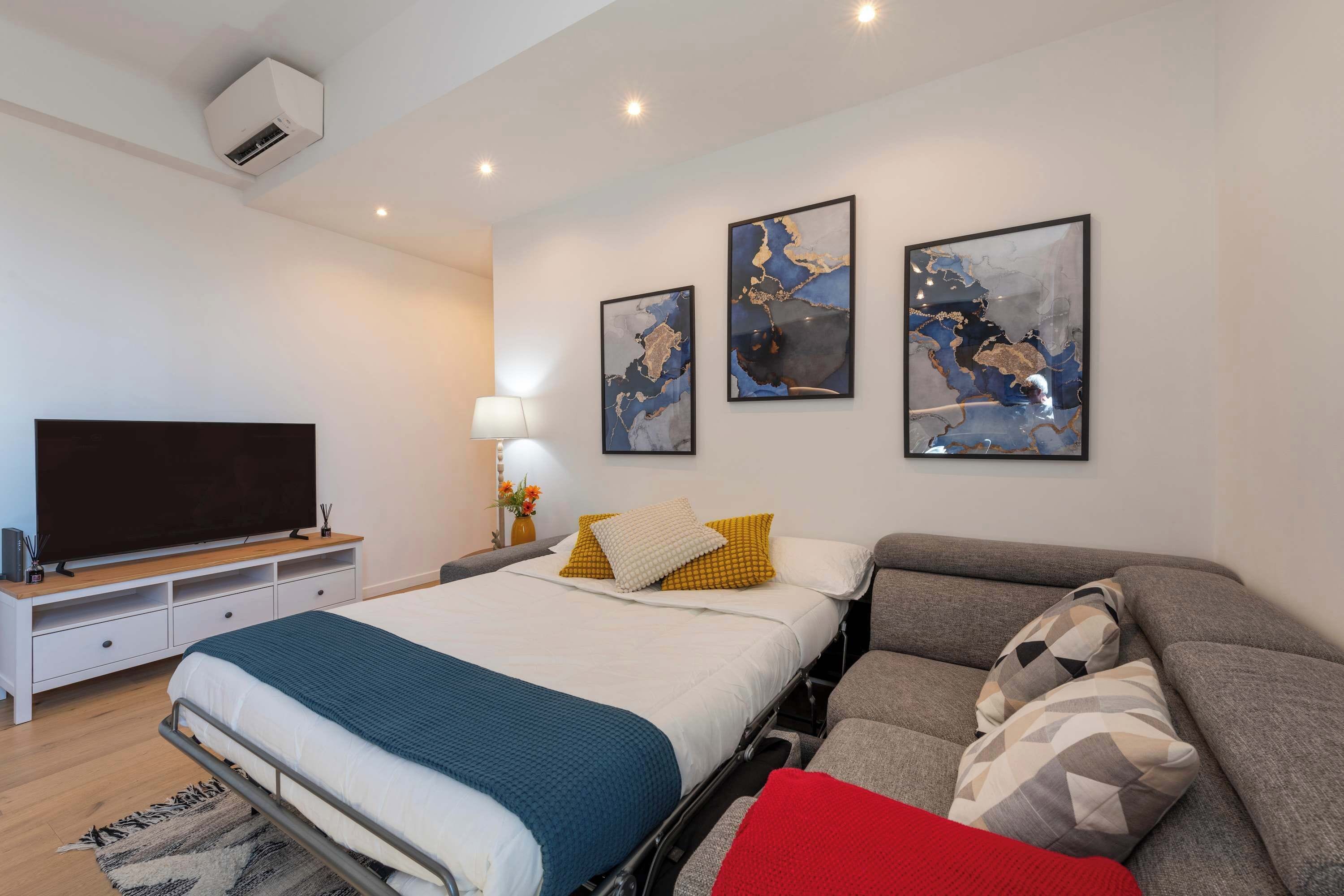 Une chambre moderne avec un lit, un canapé, un téléviseur et des œuvres d’art accrochées au mur.