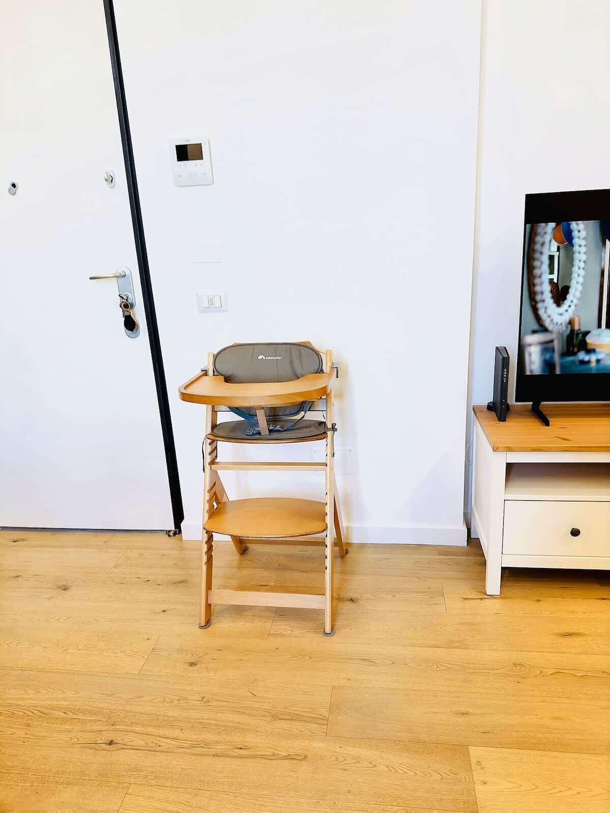 Ein Zimmer mit Holzboden, einer weißen Tür, einem Babyschaukelstuhl und einem Fernseher auf einem Holzbodenständer.