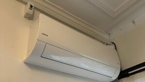 A white air conditioning unit mounted on a wall with a visible control panel and a power outlet.