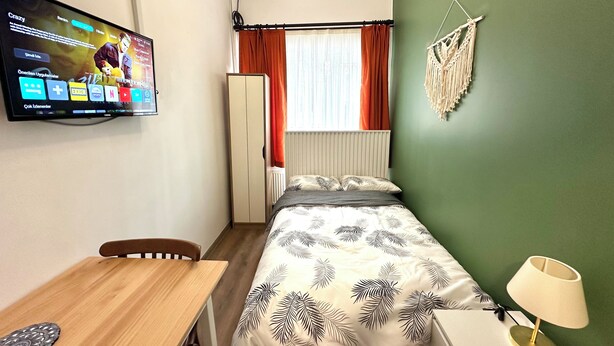 A compact hotel room with a bed, a desk, a chair, a TV, and a window with curtains.