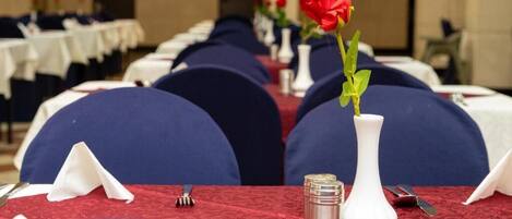 Ein Bankettsaal mit Tischen, jeder Tisch ist mit einer roten Tischdecke, weißen Servietten und Besteck gedeckt.