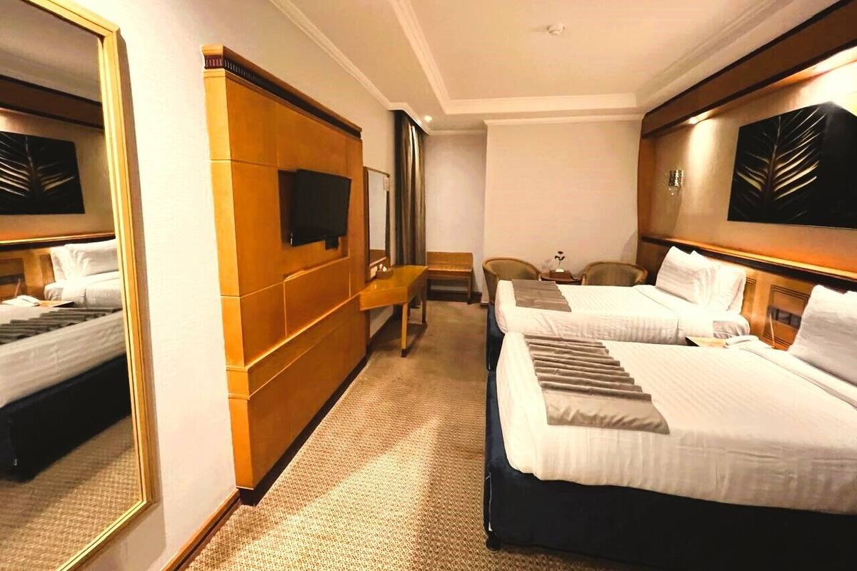 Habitación de hotel con dos camas, un espejo grande, televisor de pantalla plana y pared de paneles de madera.