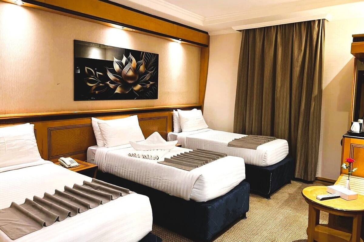 Una habitación de hotel con dos camas, una mesita de noche con un teléfono, un cuadro en la pared y una cortina.