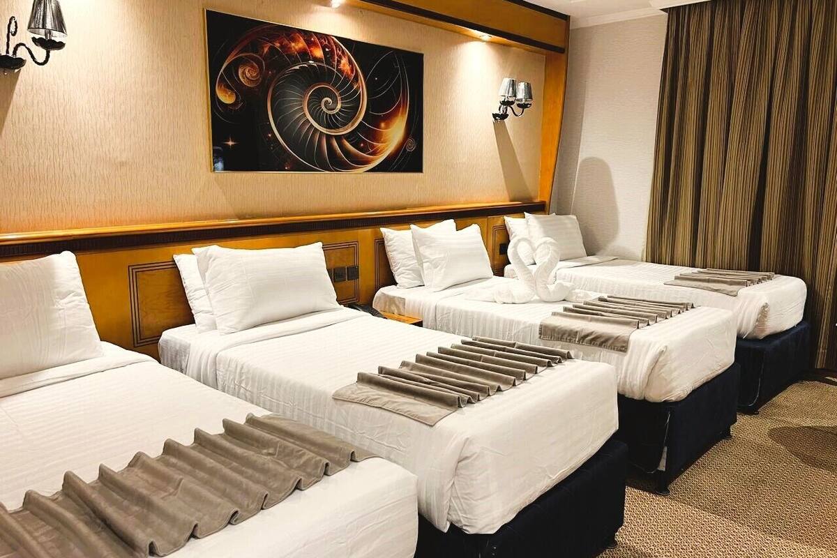 Habitación de hotel con cuatro camas individuales, un cuadro abstracto grande en la pared y una cortina en la ventana.
