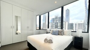 A modern hotel room with a large bed, white wardrobe, and a city view through large windows. - High Floor 2BR2Bath in Prime CBD (Melbourne)