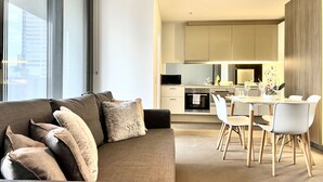 A modern living room with a sofa and chairs, a dining area with a table and chairs, and a kitchen with cabinets and appliances. - High Floor 2BR2Bath in Prime CBD (Melbourne)