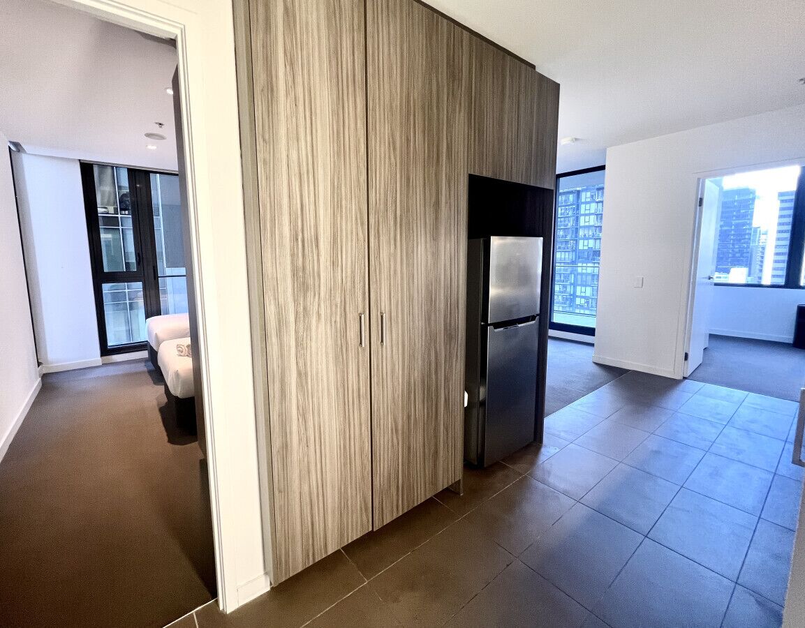 A modern apartment with a large sliding door, a built-in refrigerator, and a view of a cityscape through large windows.