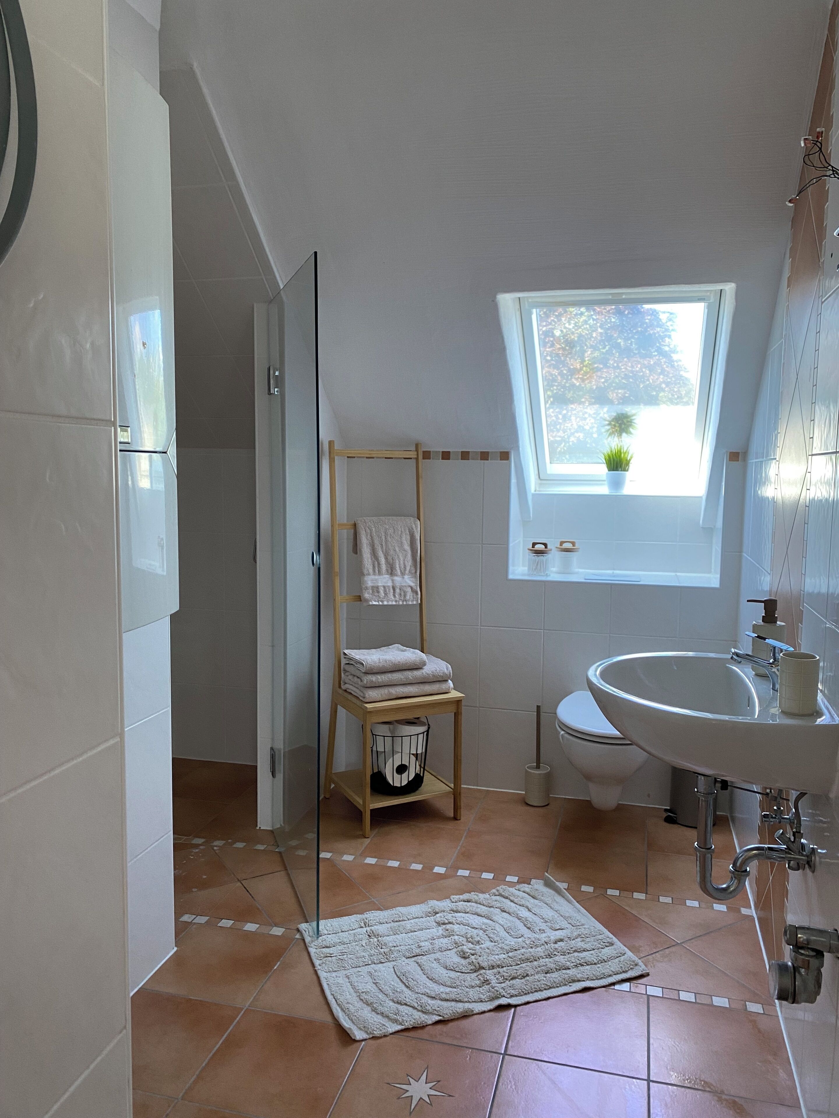Ein Badezimmer mit Fenster, Waschbecken, Handtuchhalter und Duschbereich.