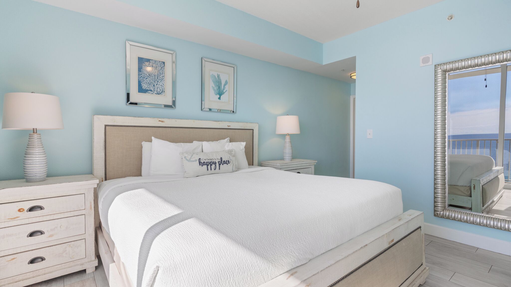 A bedroom with a large bed, two bedside tables, a dresser, and a large mirror.