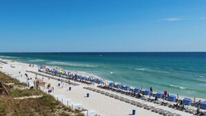 A beach with rows of striped beach umbrellas and lounge chairs, a pier in the background, and a clear blue sky. - *Oct 10 - 18th Getaway! * Beach Chairs! (Panama City Beach)